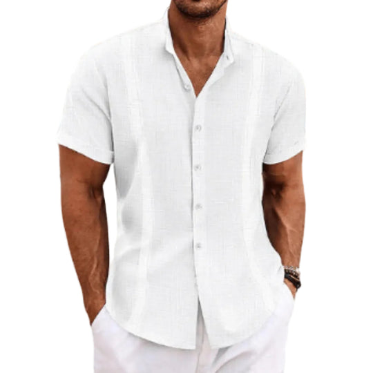 Man wearing a white short-sleeve shirt on a beach with ocean and sky in the background