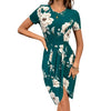 Woman wearing a teal floral dress against a white brick wall.