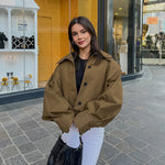 Woman wearing a khaki lapel simple single-breasted coat with drop-shoulder sleeves, paired with white pants.