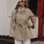 Khaki women's trench coat with long sleeves and lace-up details, styled with accessories in an urban setting.