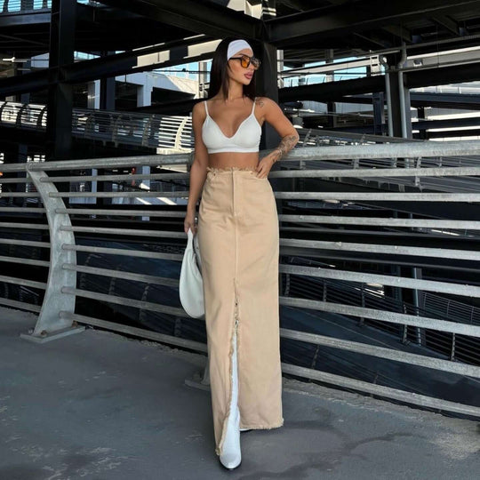 Woman in a white top and khaki skirt posing in an urban setting, showcasing summer fashion trends.