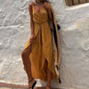 Fashionable woman in a caramel solid color jumpsuit with a wrap design and a side slit against a textured wall.