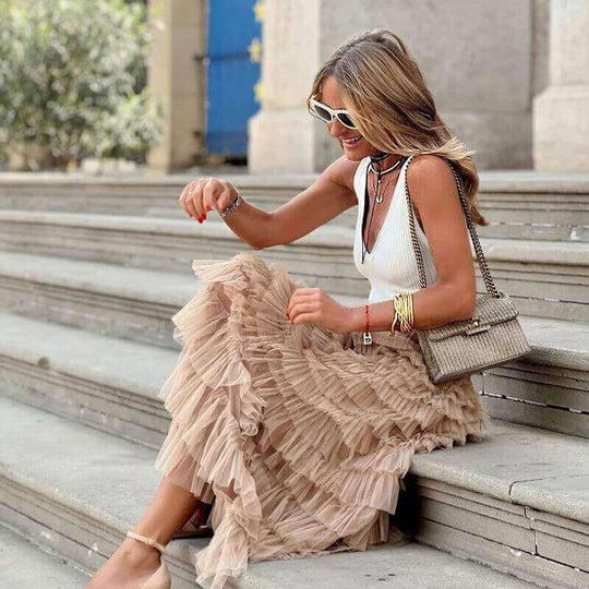 Woman in layered khaki ruffles cake skirt, stylish summer fashion, sitting on steps and smiling.