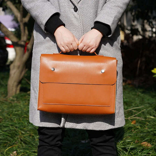 Stylish tan PU leather laptop handbag held by a person in casual attire, showcasing its elegant design outdoors.