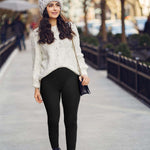 Stylish woman in black one-piece yoga leggings walking outdoors in a cozy sweater and hat.