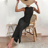 A woman sitting on a chair wearing a knitted hollow bikini cover-up in black, accessorized with a large sun hat.
