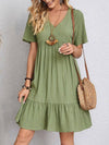 Model wearing a tiered corset V-neck dress in green with short sleeves and loose tiered skirt.