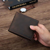 Hand holding a vintage dark brown men's wallet made of genuine leather, featuring a European retro style on a wooden table.