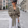 Stylish woman in olive large lapel trench coat with belt, posing outdoors in a chic urban setting.