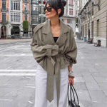 Stylish woman in olive large lapel trench coat with belt, posing outdoors in a chic urban setting.