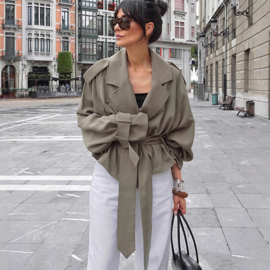 Stylish woman in olive large lapel trench coat with belt, posing outdoors in a chic urban setting.