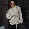 Light khaki loose waistband trench coat with long sleeves, stylishly paired with sunglasses and a handbag.