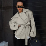 Light khaki loose waistband trench coat with long sleeves, stylishly paired with sunglasses and a handbag.