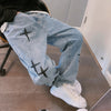 Casual blue nine point jeans with artistic black cross designs, worn by a person sitting in a stylish indoor setting.